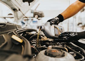 Close-up of a mechanic pouring engine oil into a car engine in an auto repair shop.