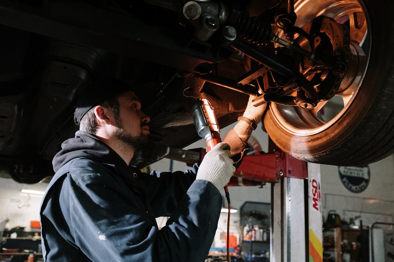 Mechanic examining car's undercarriage at a garage, focusing on vehicle maintenance.