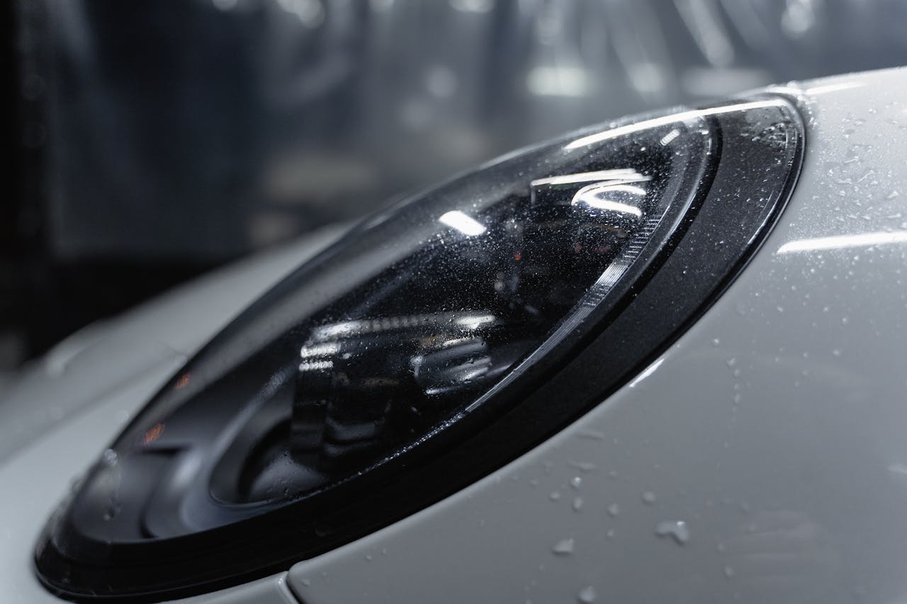 Detailed shot of a sleek car headlight with water droplets enhancing its glossy surface.