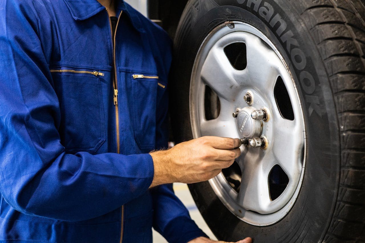 Mechanic in blue coveralls inspecting a car tire in an auto repair workshop.